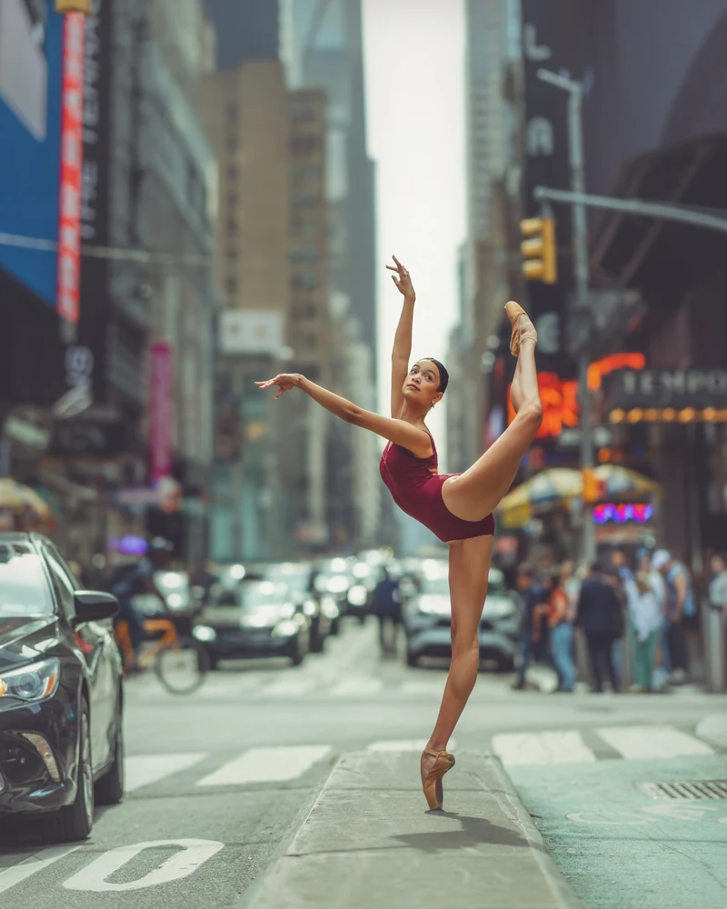 Grace in a burgundy leotard extending one leg beside a New York crosswalk