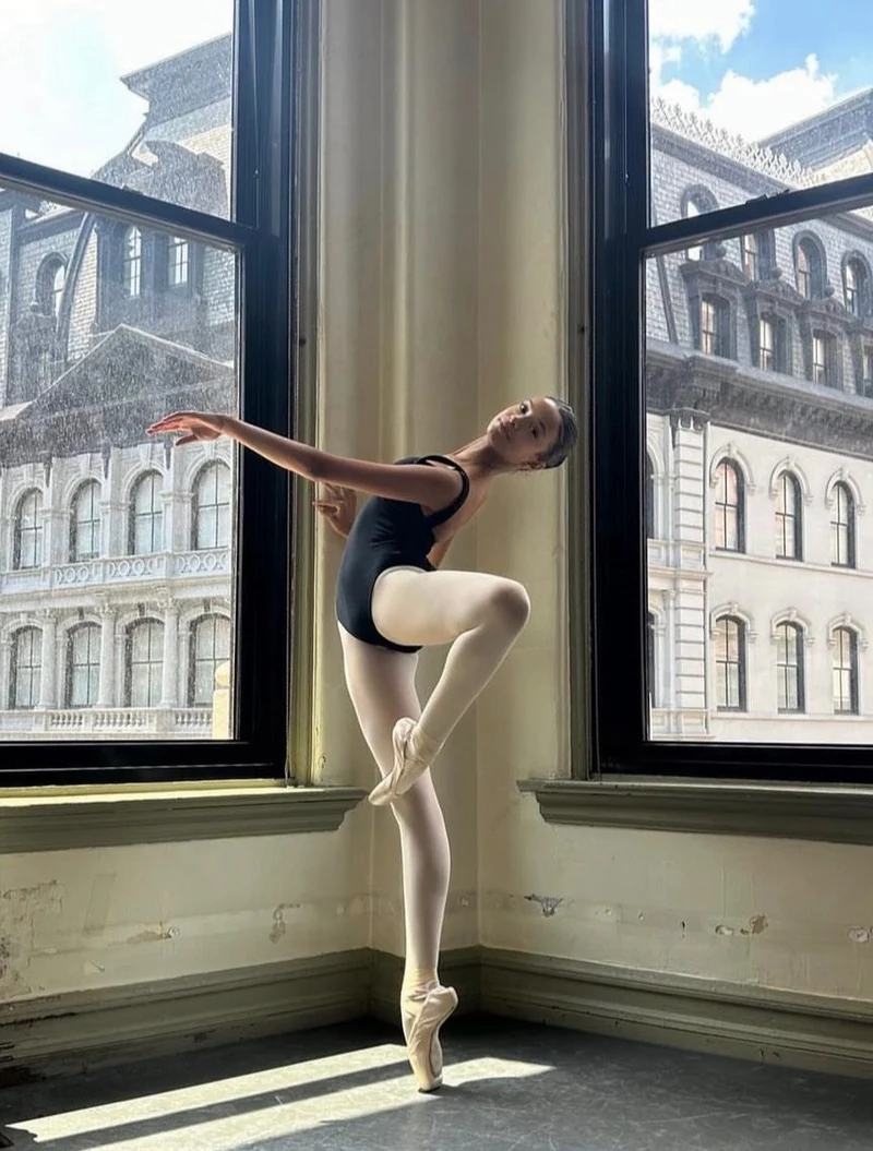 Grace en pointe in a black leotard between sunlit studio windows