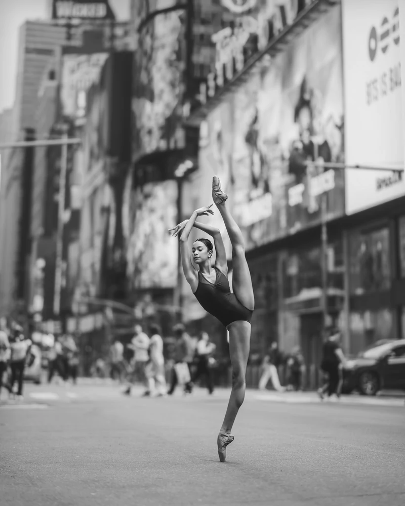Grace en pointe with one leg extended overhead in Times Square, photographed in black and white