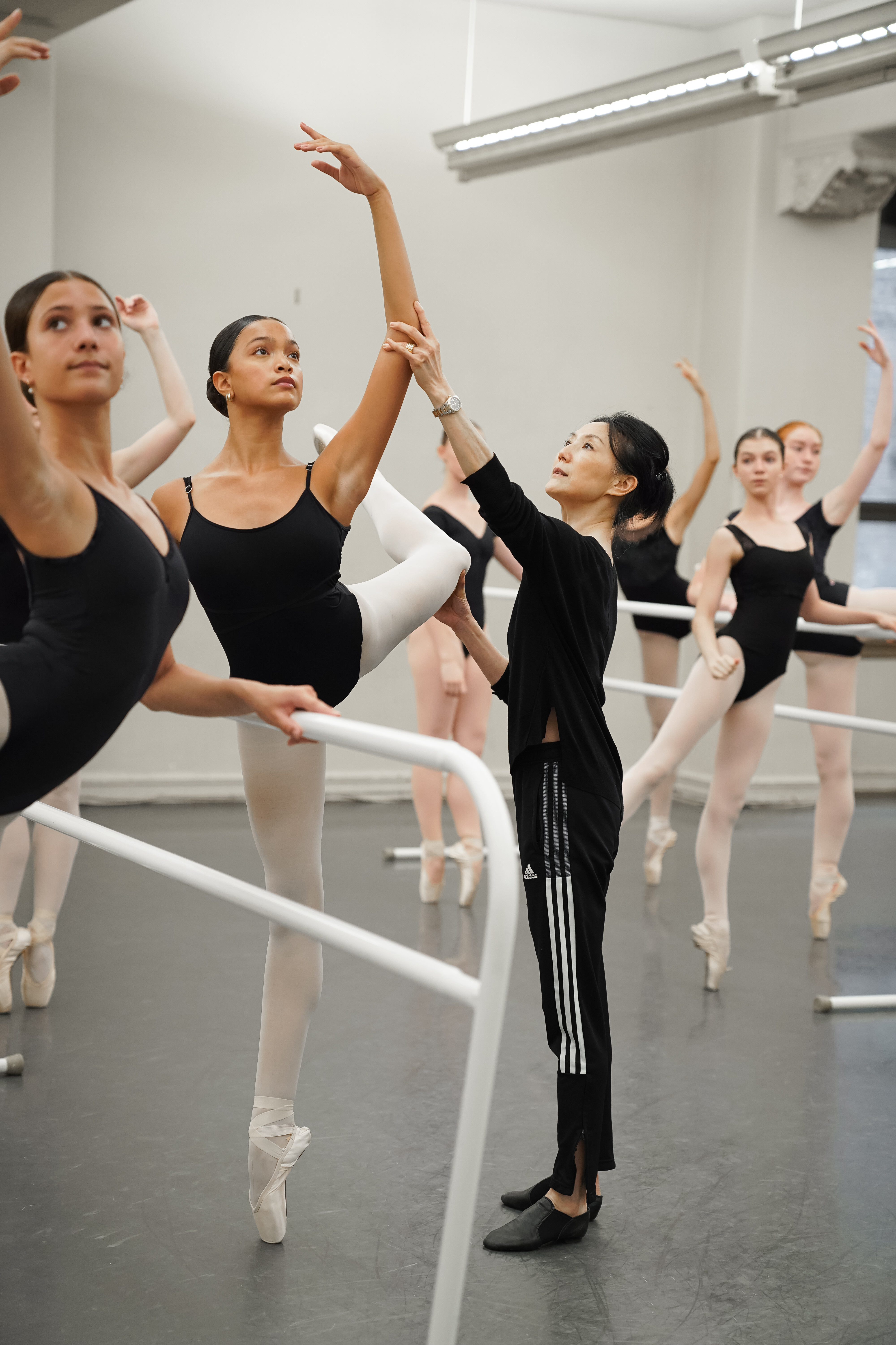A ballet teacher guiding a student’s arm placement during pointe class